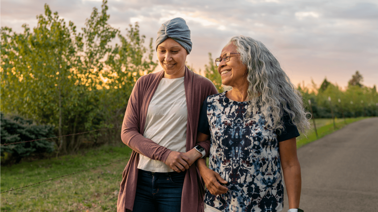Two women, one who's undergoing cancer treatment, walking together with linked arms.