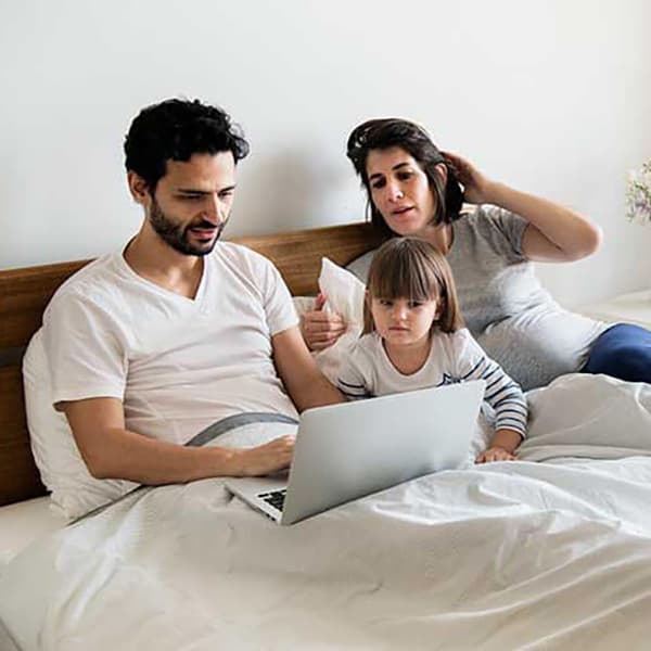 Mom, dad and kid watching laptop on bed.
