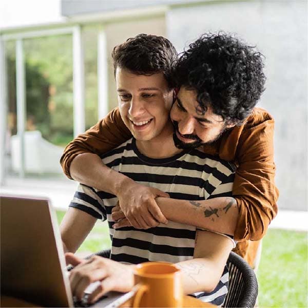 Man hugging his partner who is on his laptop.