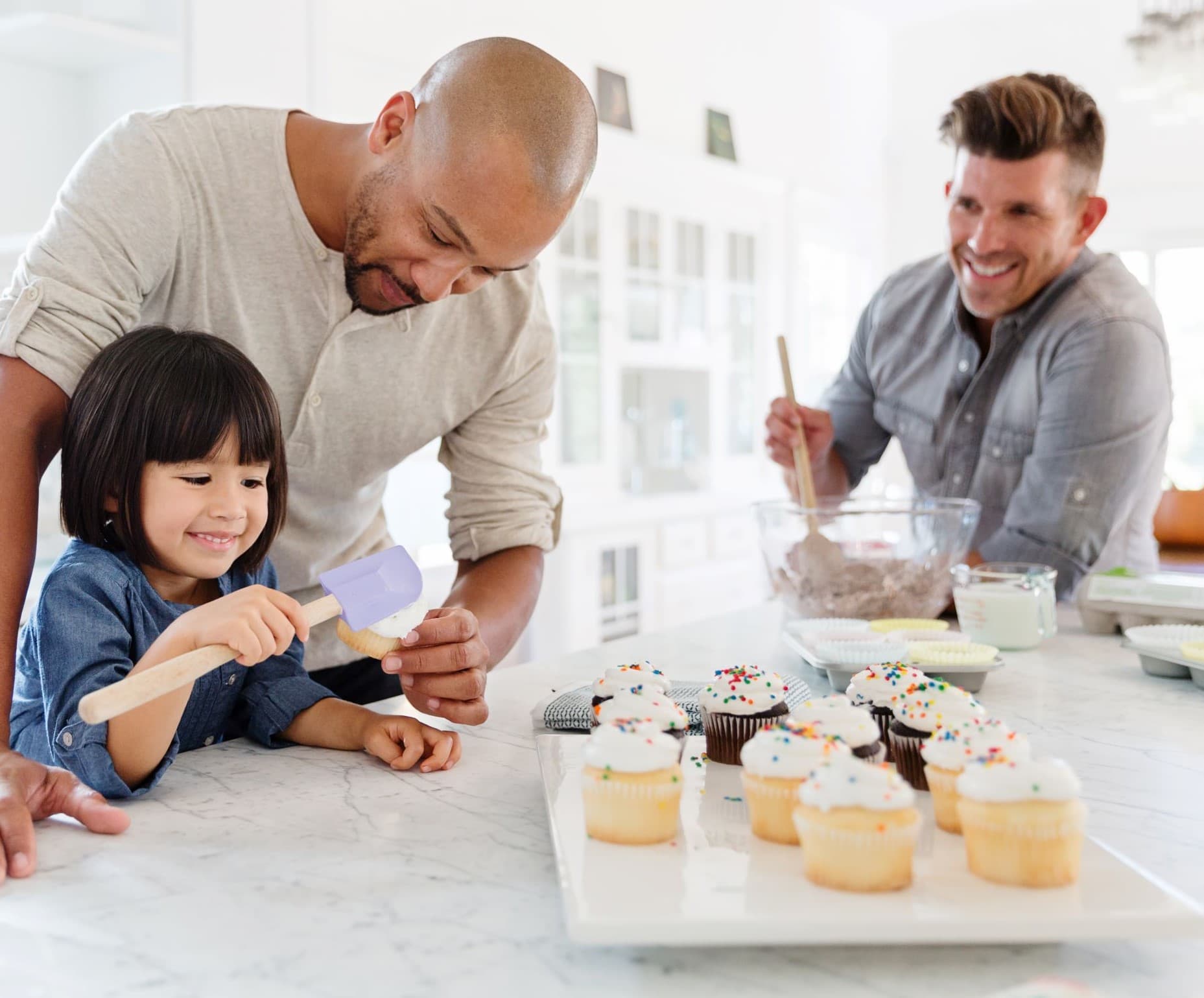 Two men bake cupcakes with a young girl.