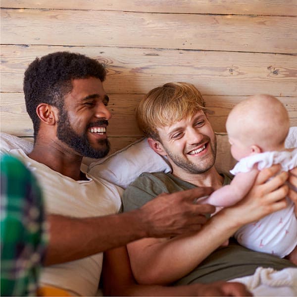 Two dads playing with their newborn baby.