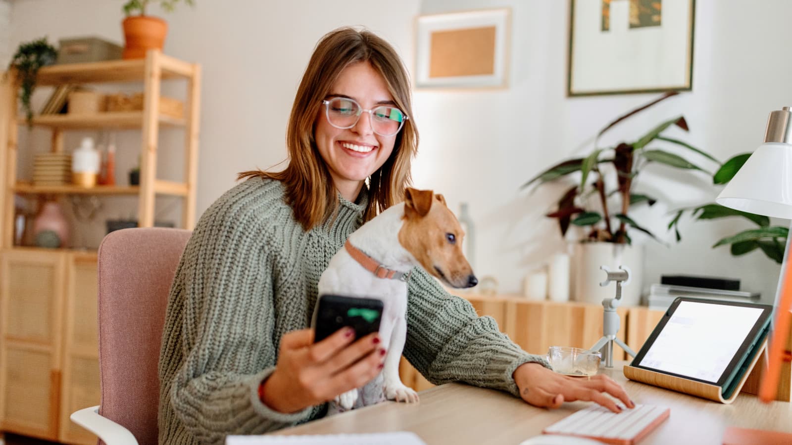 Smiling young woman at desk with dog viewing phone