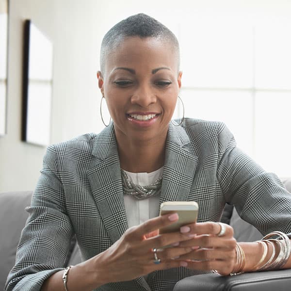 Black female business manager sitting on a couch using her phone.