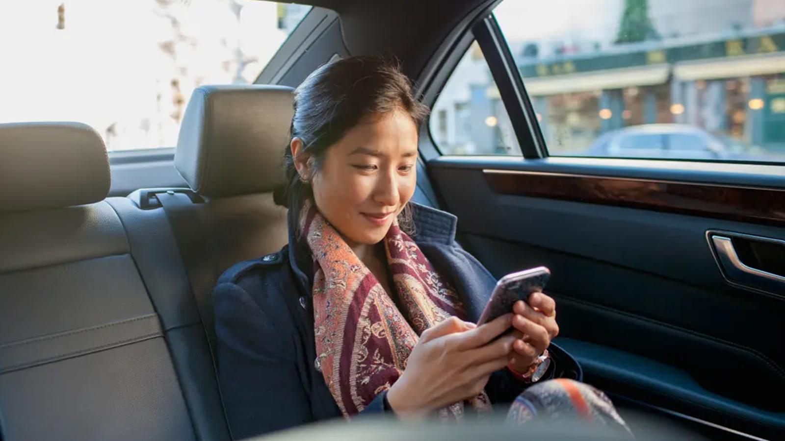 Woman checking her phone in the back seat of a car.