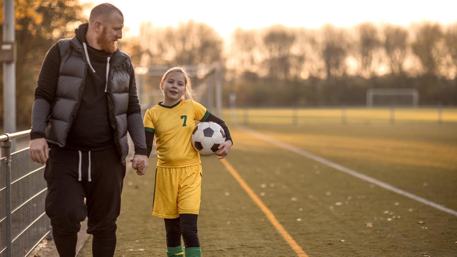 Father holding his daughter's hand after her soccer game Father holding his daughter's hand after her soccer game