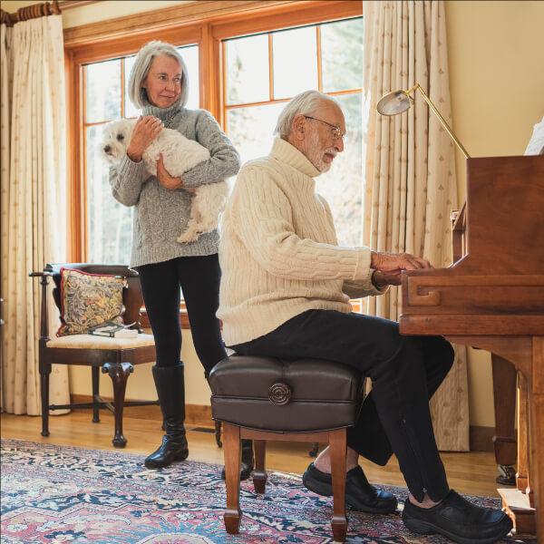 Woman holding a dog and a man playing piano.
