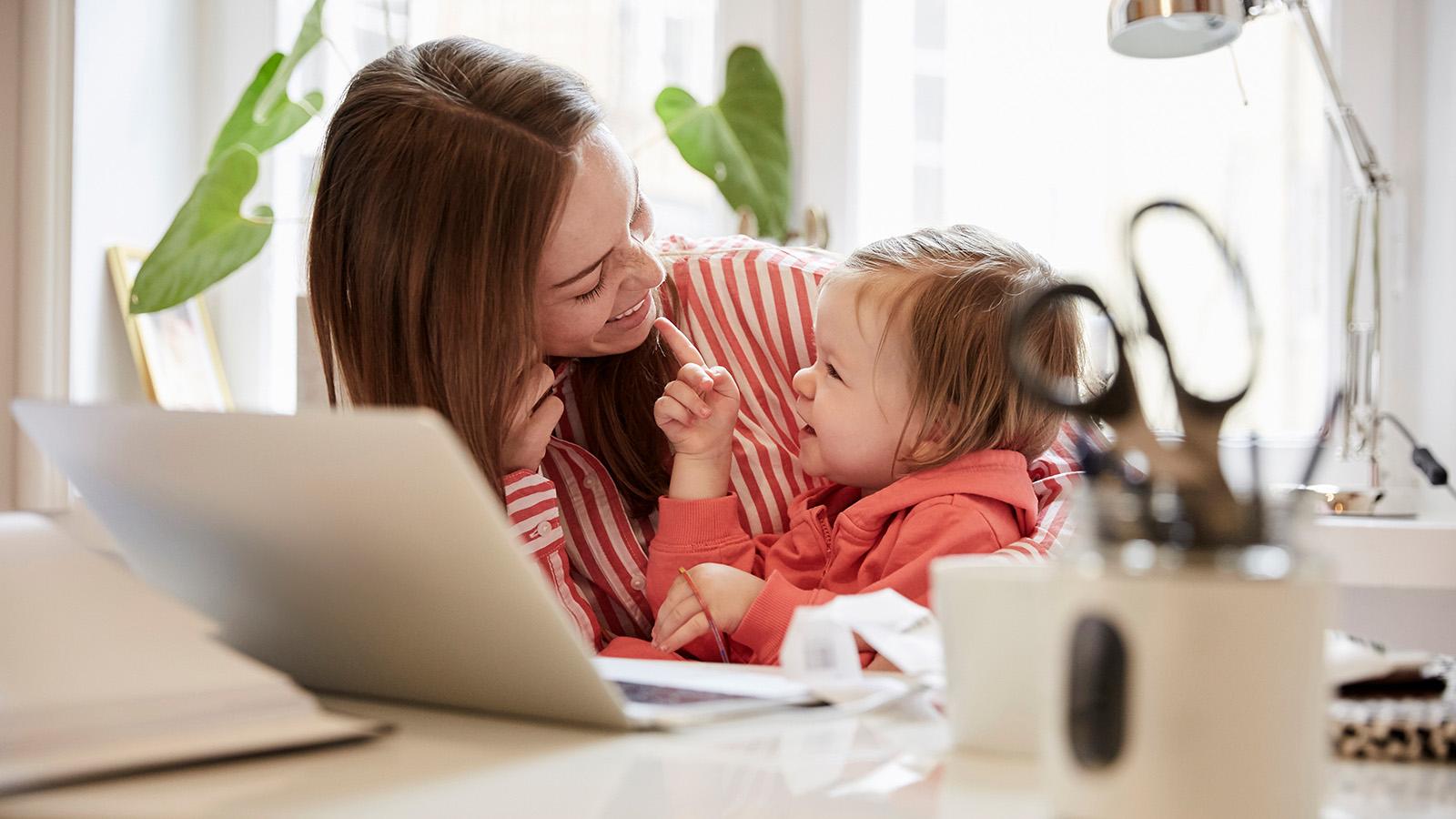 Mother working at home and holding her daughter
